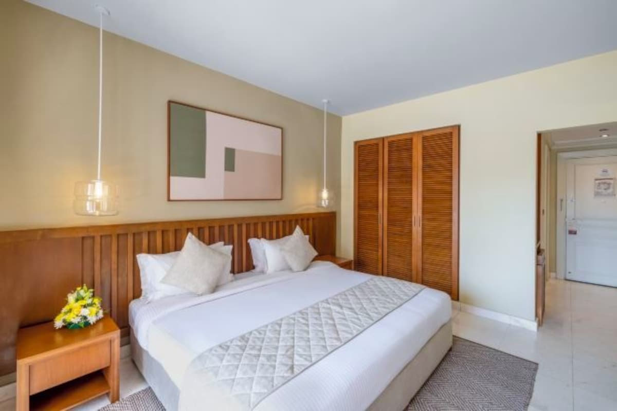 Une chambre d’hôtel avec un grand lit, une tête de lit en bois, des tables de chevet, un tableau encadré au mur et une armoire.