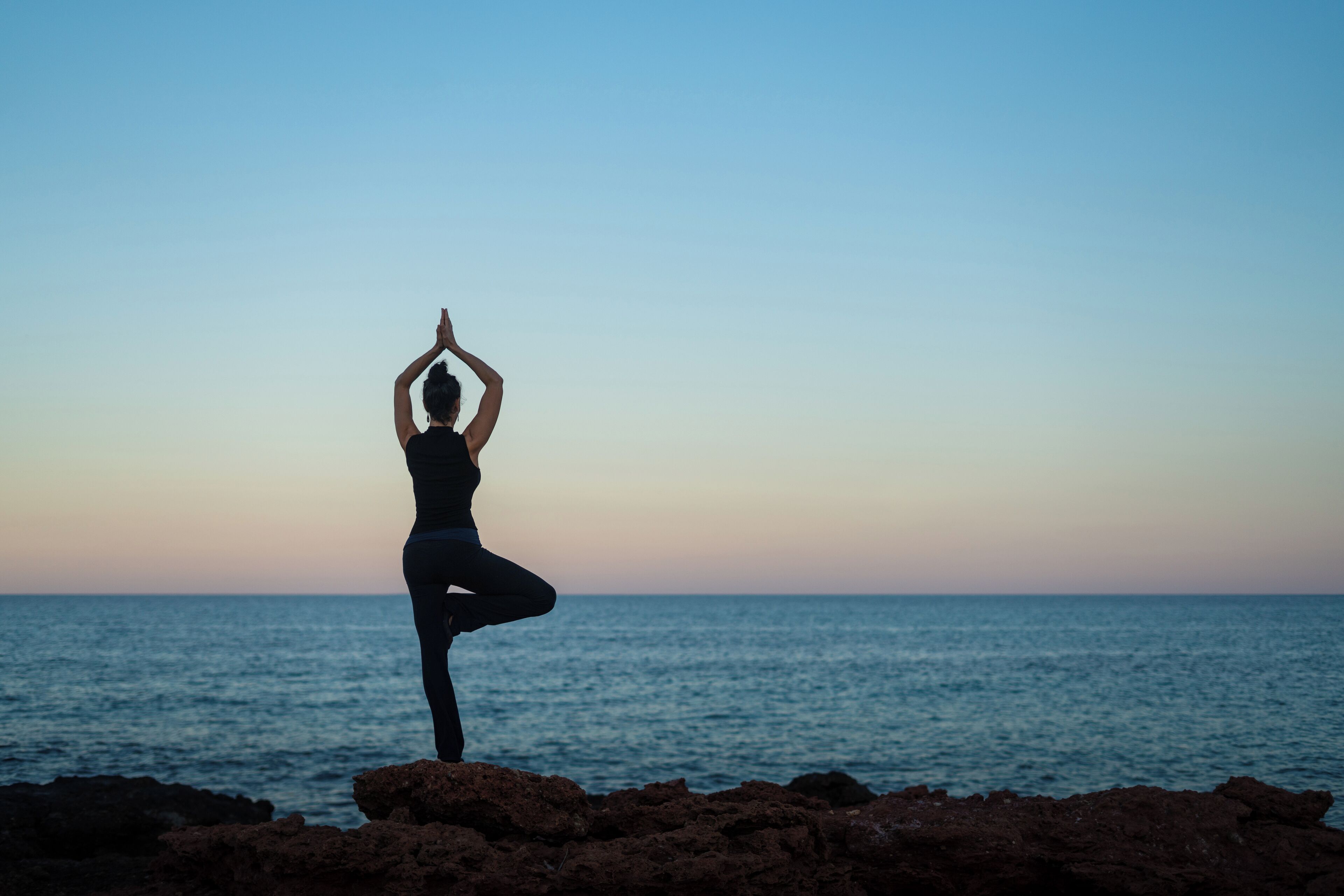 A person performing a yoga pose on a rocky shoreline with a view of the ocean.