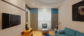 Ein modernes Wohnzimmer mit Fernseher, grauem Sessel, blauem Sofa und Couchtisch aus Holz.