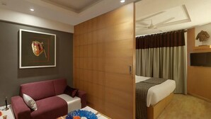 Ett hotellrum med en säng, en röd soffa, en trägarderob, en takfläkt, en tv och en inramad tavla på väggen.