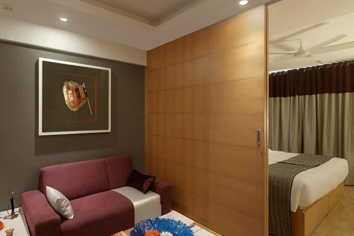 Habitación de hotel con una cama, un sofá rojo, un armario de madera, un ventilador de techo, un televisor y un cuadro en la pared.