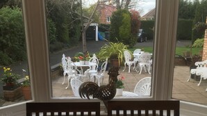 A dining area with a table set for two, a decorative rooster centerpiece, and a view of the outdoor patio with white chairs and potted plants. - Elmdon Lodge (Birmingham)
