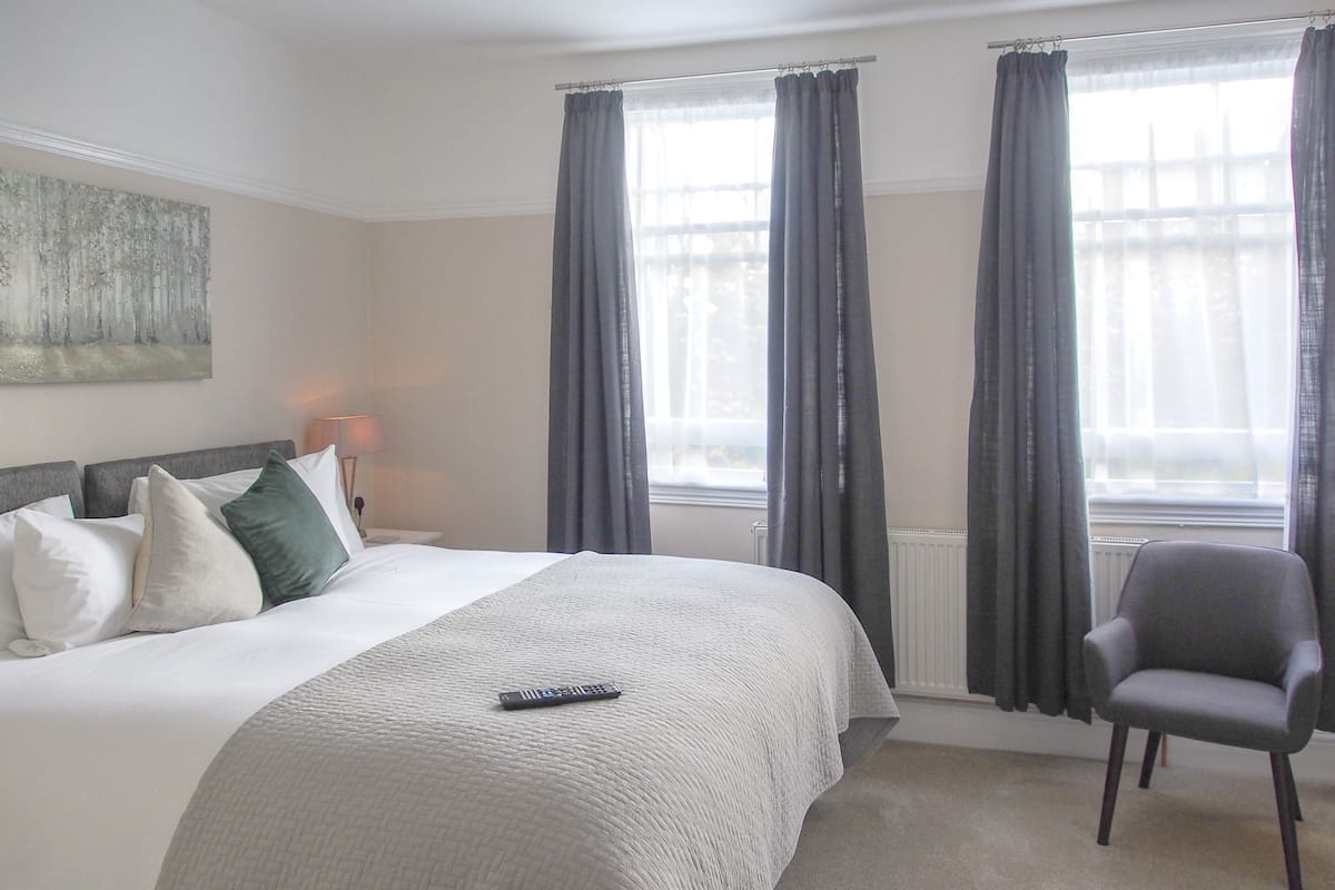 A hotel room with a large bed, a chair, a lamp, and a window with curtains.