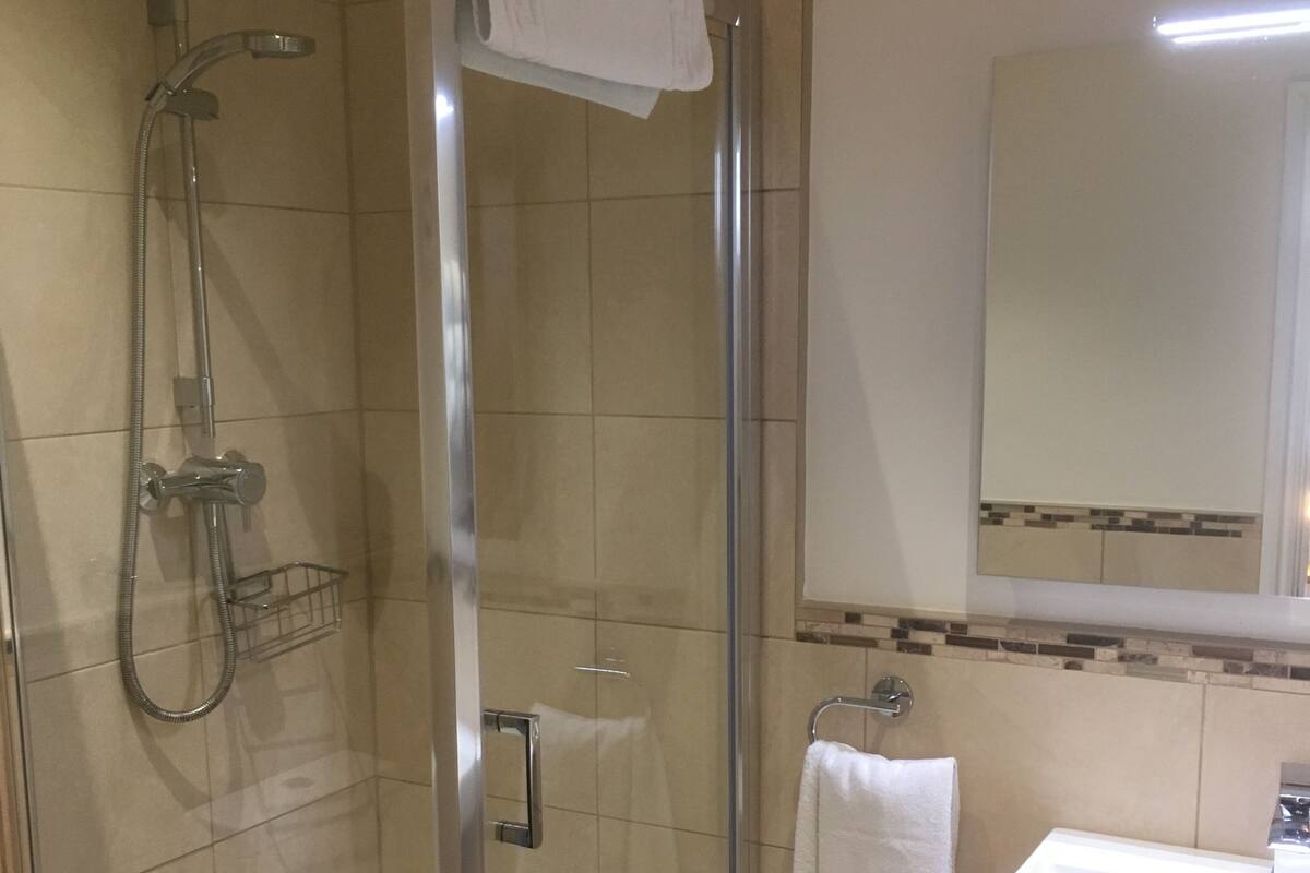 A glass-enclosed shower with a handheld showerhead, a glass door, and a white towel hanging on the door.