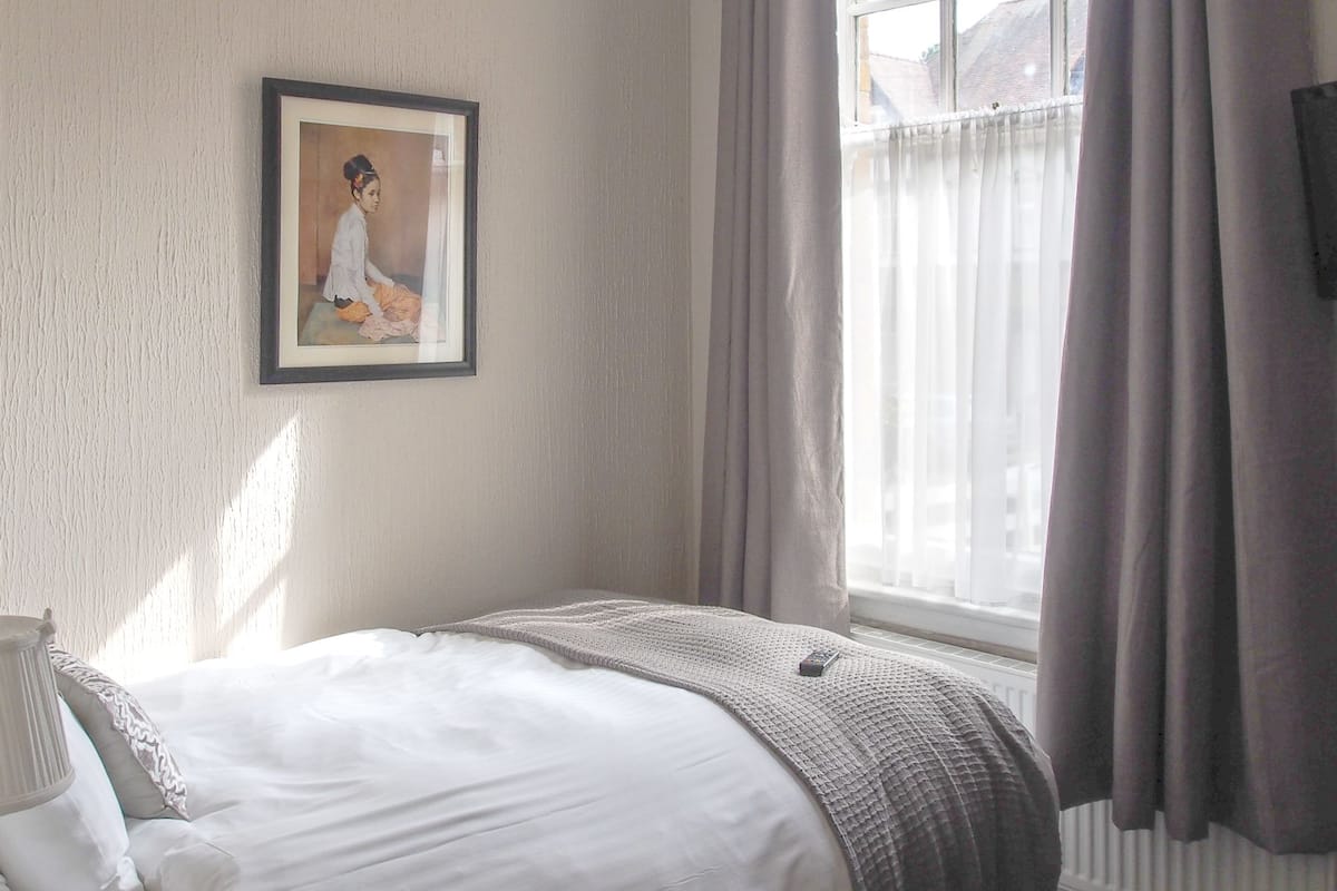 A bedroom with a bed, a framed picture on the wall, and a window with curtains.
