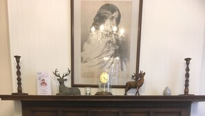 A fireplace with a mantel decorated with a clock, a deer figurine, and a framed picture. - Elmdon Lodge (Birmingham)