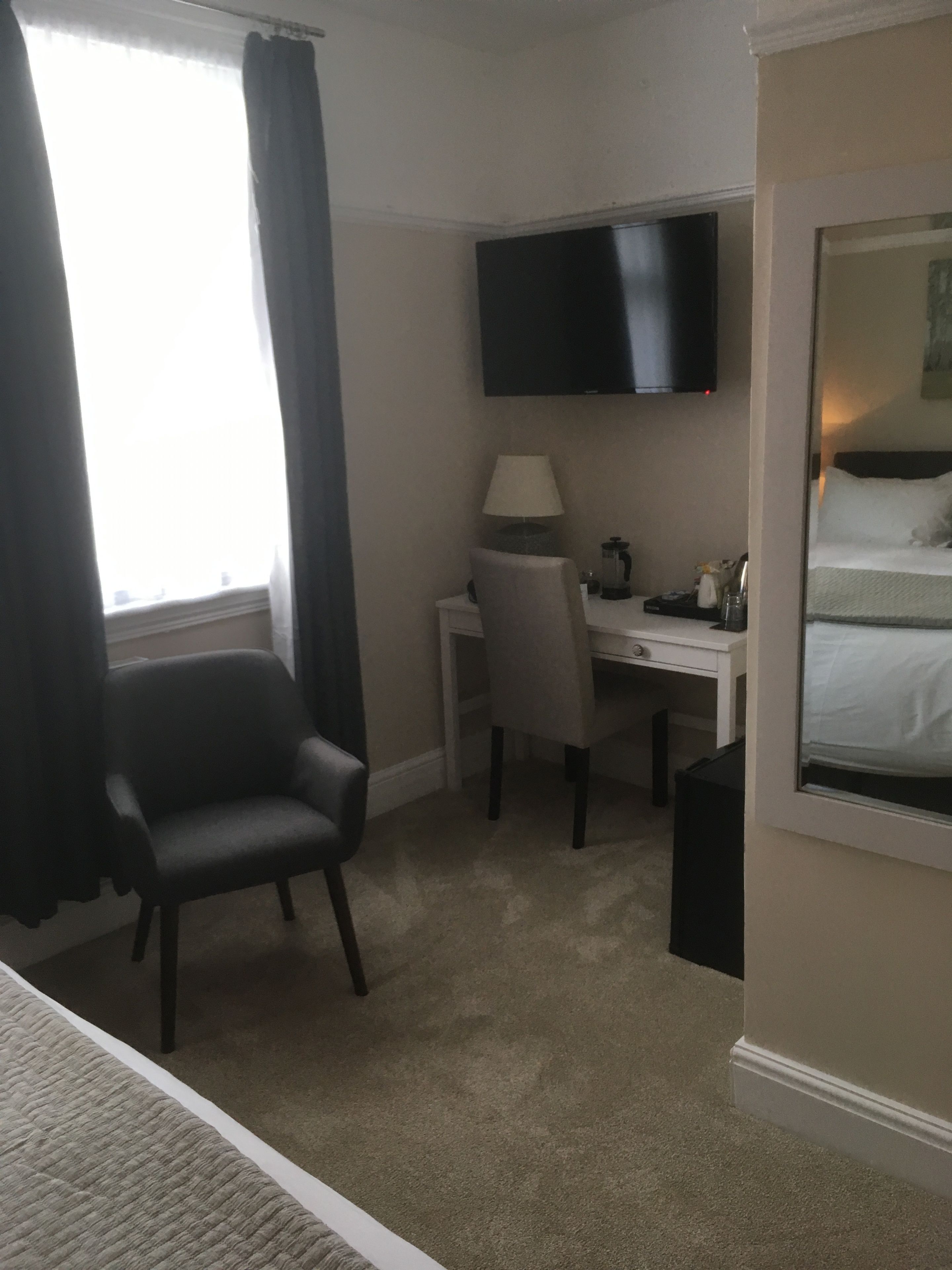 Ein Hotelzimmer mit Bett, Schreibtisch, Stuhl, Fernseher und einem fensterbepflanzten Fenster.