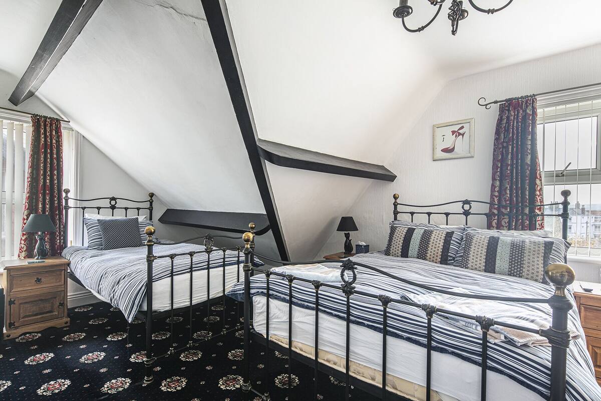 A bedroom with a sloped ceiling, a bed with striped bedding, a nightstand, a lamp, and a window with curtains.
