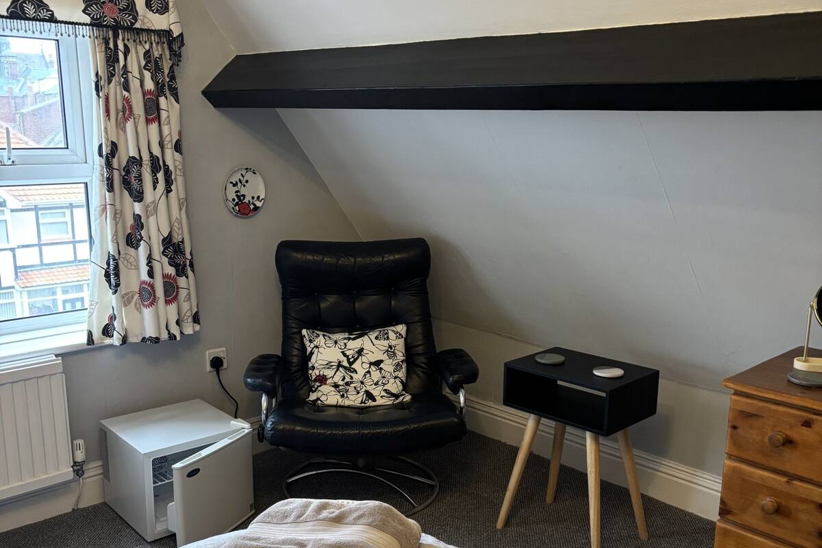 A bedroom with a bed, a chair, a dresser, a heater, and a window with curtains.