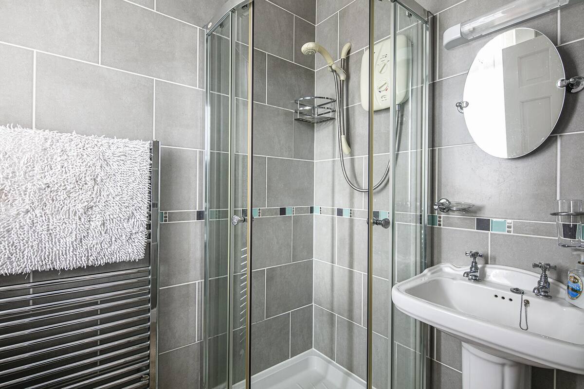 A modern bathroom with a glass-enclosed shower, a white sink with a mirror, and a towel rack.