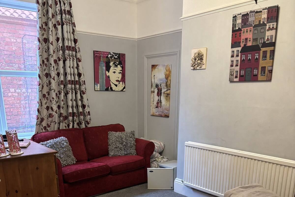 A bedroom with a red sofa, a striped bed, a wooden dresser, and a radiator.