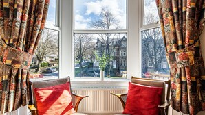 A room with two chairs facing a large window with patterned curtains. - Fountains Guest House (Harrogate)