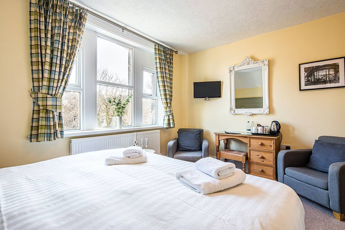 Ett hotellrum med en stor säng, två fåtöljer, en byrå, en spegel och ett fönster med gardiner.