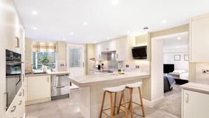 A modern kitchen with a central island, stainless steel appliances, and wooden stools. - Fountains Guest House (Harrogate)