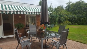 Un patio exterior con una mesa y sillas, un toldo a rayas y un muro de ladrillo.
