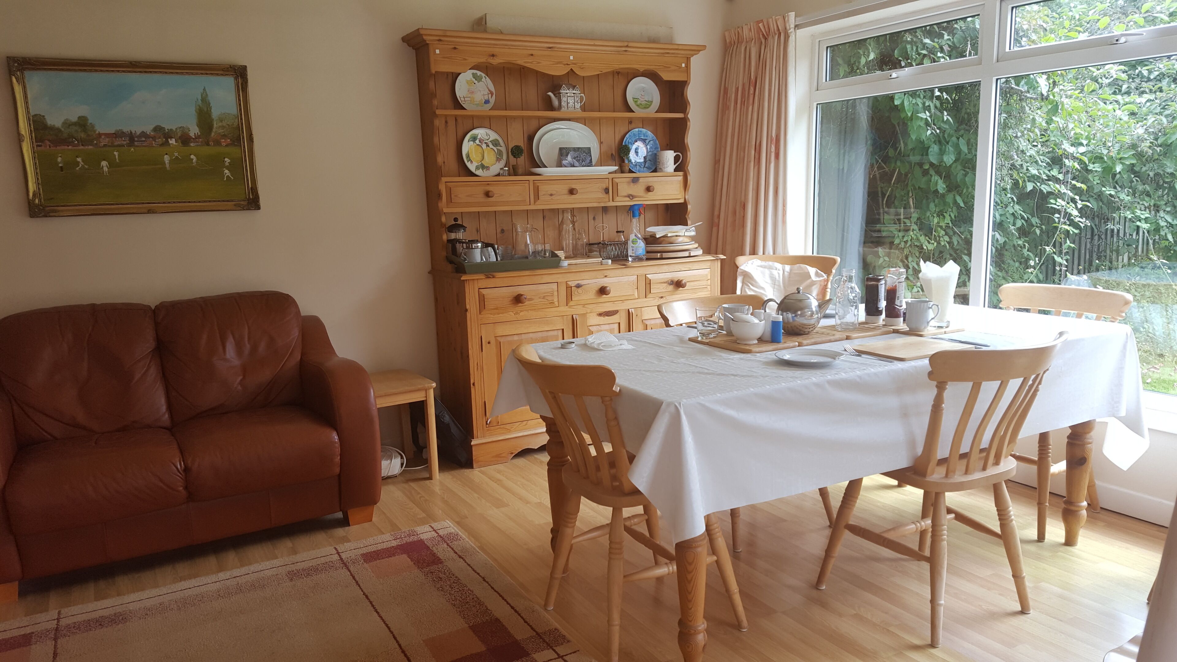 A cozy living room with a brown leather sofa, a dining table set for four, and a wooden cabinet with dishes.