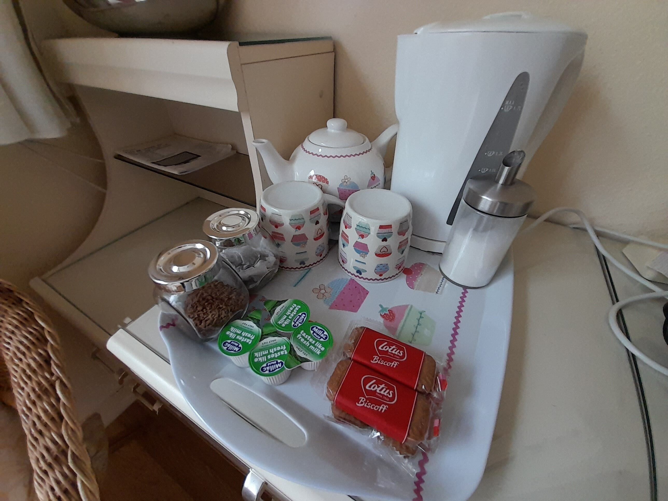 A kitchenette with a coffee maker, teapot, mug, jars, and packaged food items.