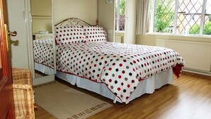 Un dormitorio con cama, una mesita de noche, una silla de mimbre y una ventana con vistas al verdor.