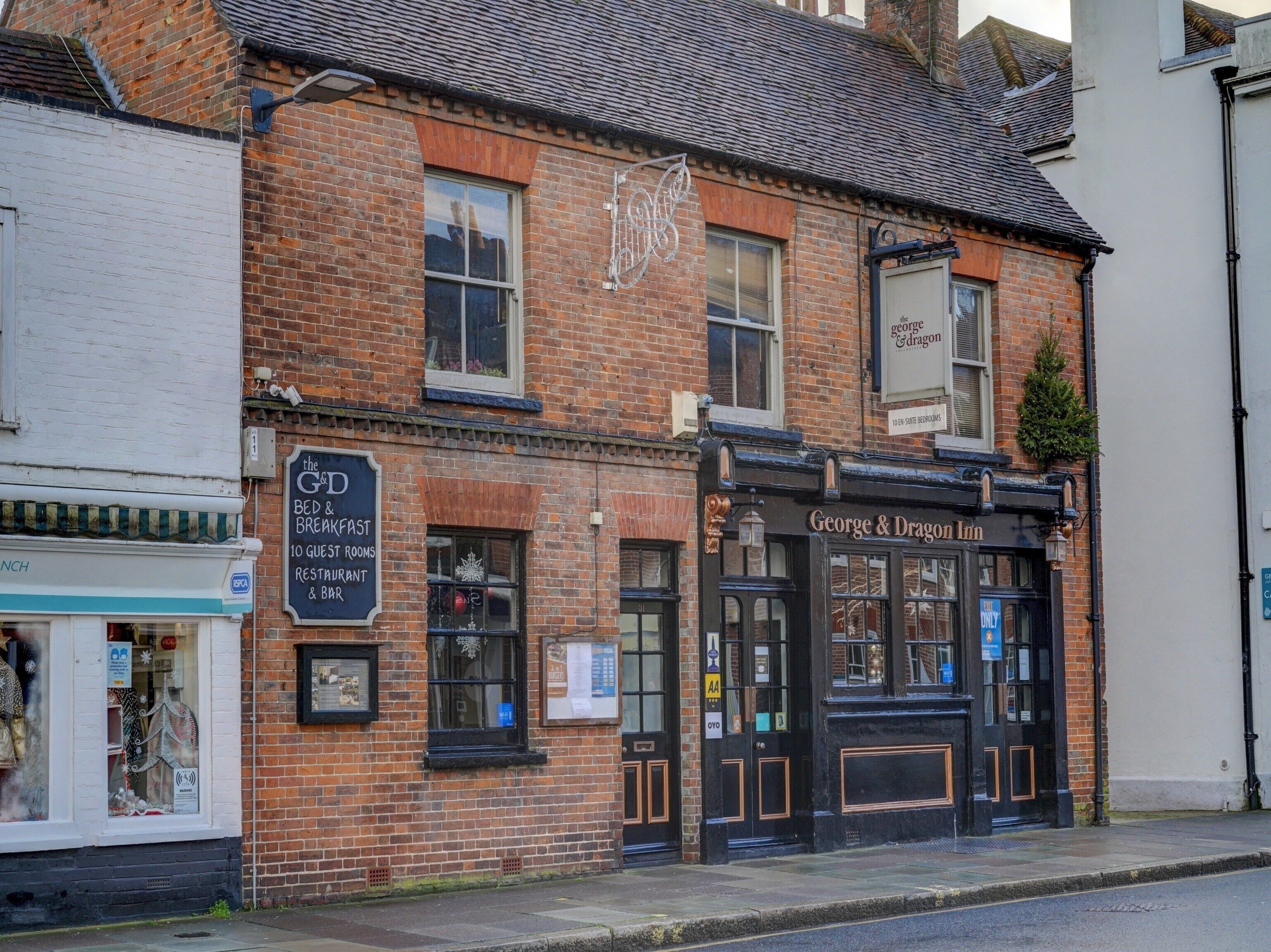 Um edifício de tijolos tradicional com fachada preta, exibindo uma placa com a inscrição 'George & Dragon Inn' e uma placa menor para 'The G&D Bed & Breakfast' com quartos de hóspedes e um restaurante/bar.