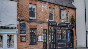 Um edifício de tijolos tradicional com fachada preta, exibindo uma placa com a inscrição 'George & Dragon Inn' e uma placa menor para 'The G&D Bed & Breakfast' com quartos de hóspedes e um restaurante/bar.