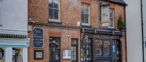 A traditional brick building with a black facade, featuring a sign for 'George & Dragon Inn' and a smaller sign for 'The G&D Bed & Breakfast' with guest rooms and a restaurant/bar.