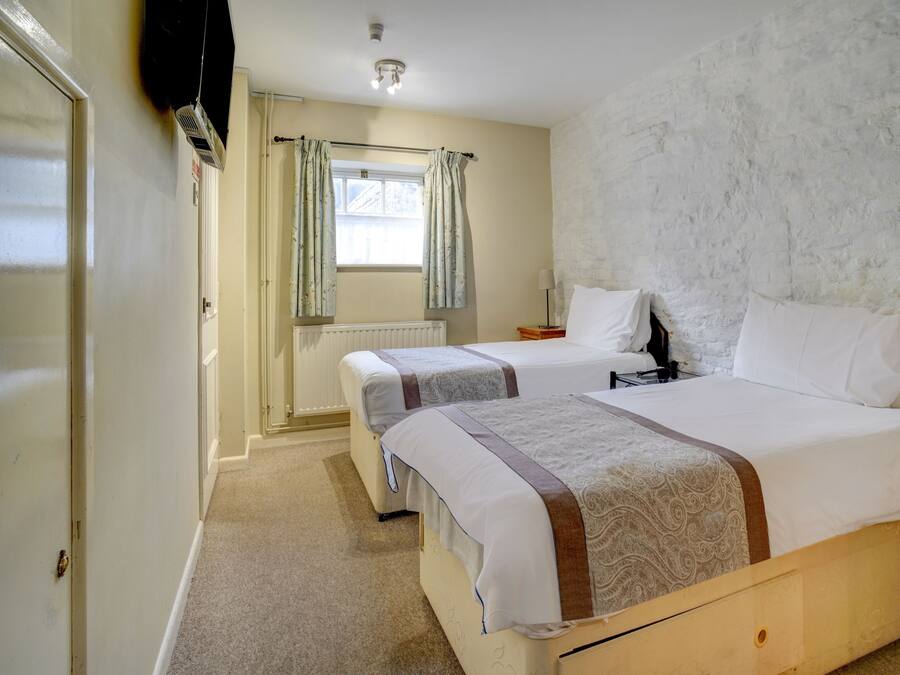 A hotel room with two beds, a radiator, a window with curtains, and a lamp on a bedside table.
