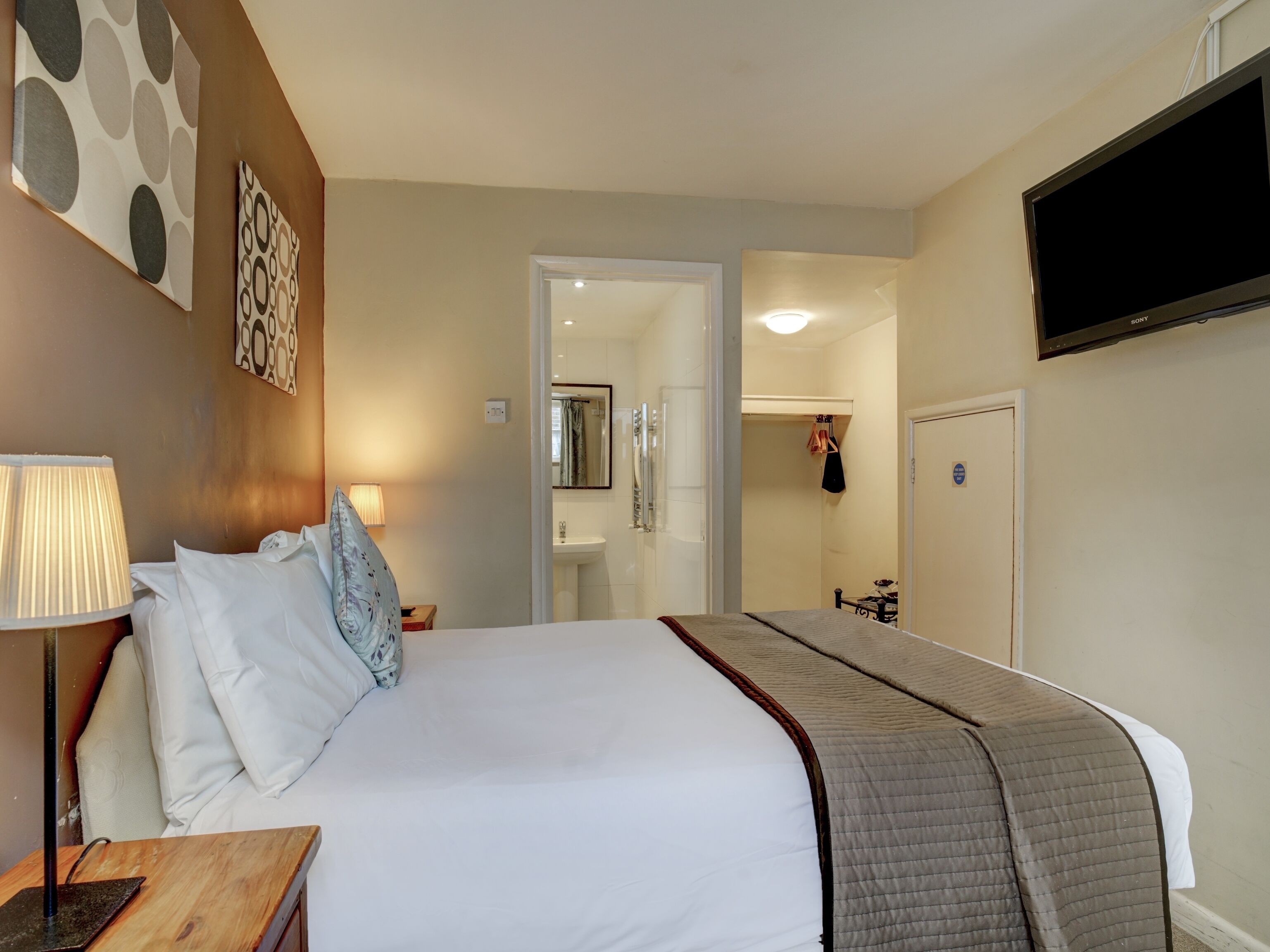Een hotelkamer met een groot bed, een bedlamp, een flatscreen-tv en een badkamer die door een geopende deur zichtbaar is.