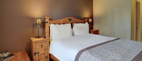 Un dormitorio con estructura de cama de madera, ropa de cama blanca, una mesita de noche con lámpara y un aparador de madera.