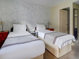 A room with two beds, each with a bedside table and lamp, against a textured wall.