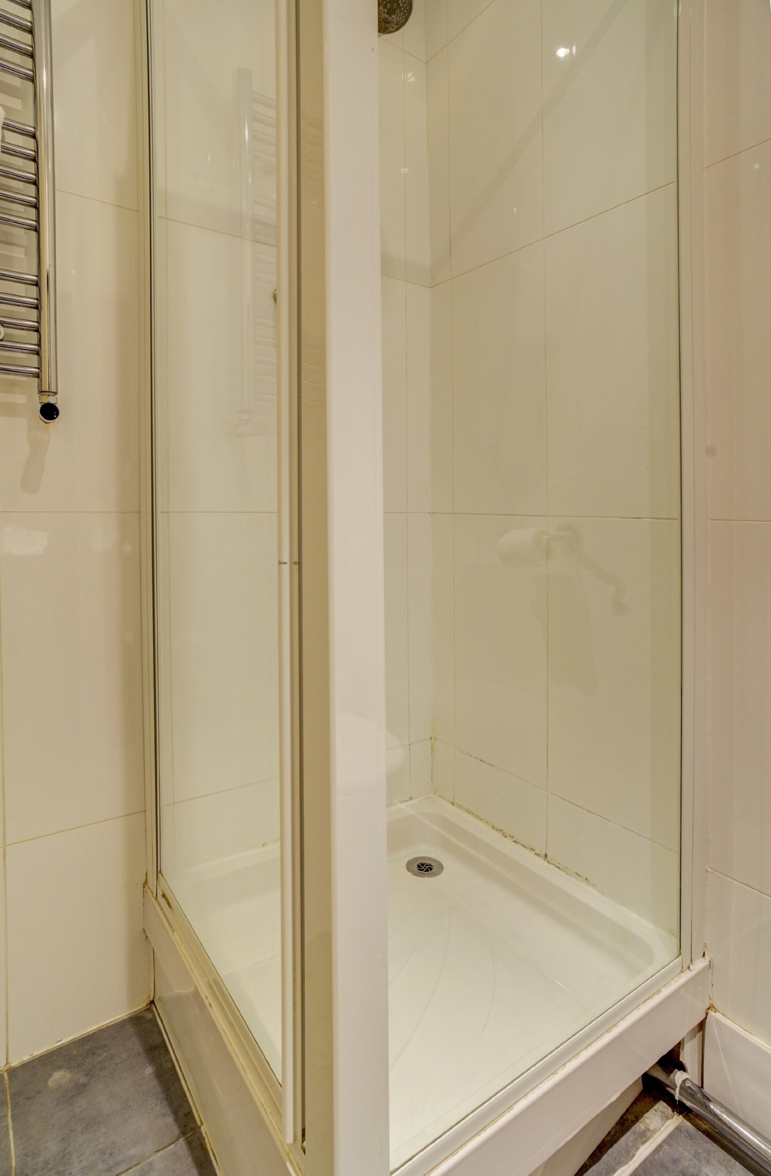 A glass-enclosed shower stall with a white tiled floor and walls.