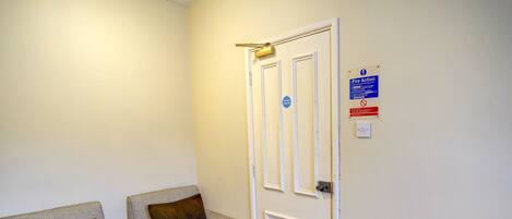 A room with two grey armchairs, a white door with a fire action sign, and a carpeted floor.