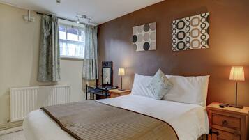 A hotel room with a bed, bedside table, lamp, and a window with curtains.