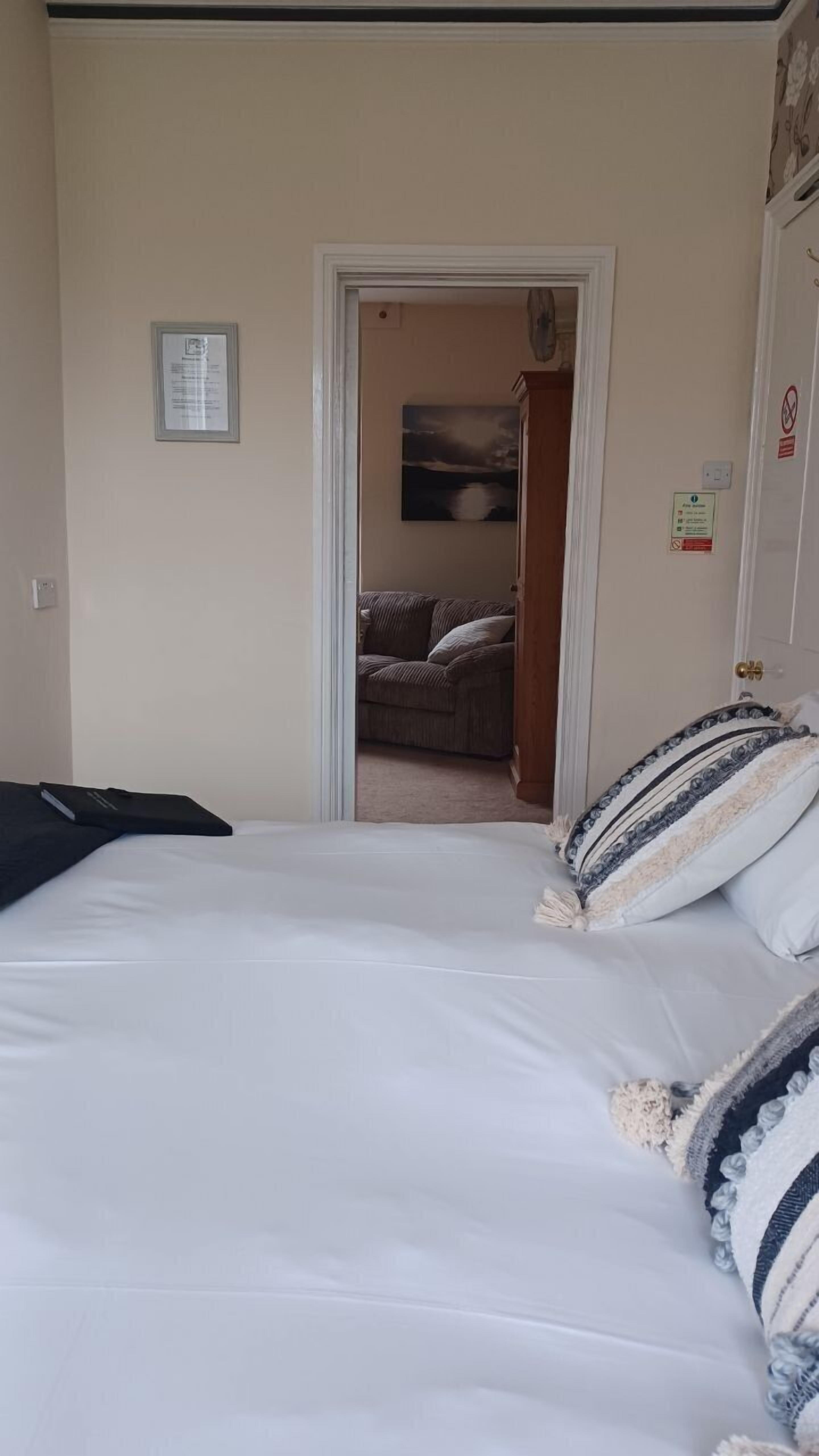 Ein Schlafzimmer mit Bett, einer Tür zu einem Wohnbereich und einem gerahmten Aushang an der Wand.