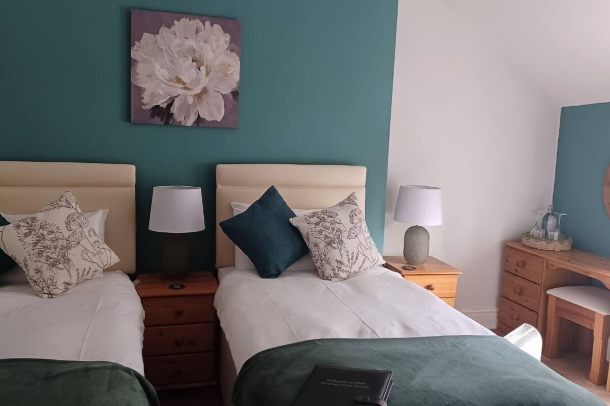 Habitación doble con dos camas, cada una con cabecero, mesitas de noche, lámparas y una obra de arte floral en la pared.