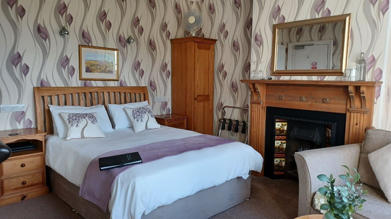 A bedroom with a wooden bed, a nightstand, a dresser, a fireplace, and a mirror.
