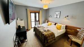 A hotel room with a bed, a desk, a chair, a lamp, and a window.