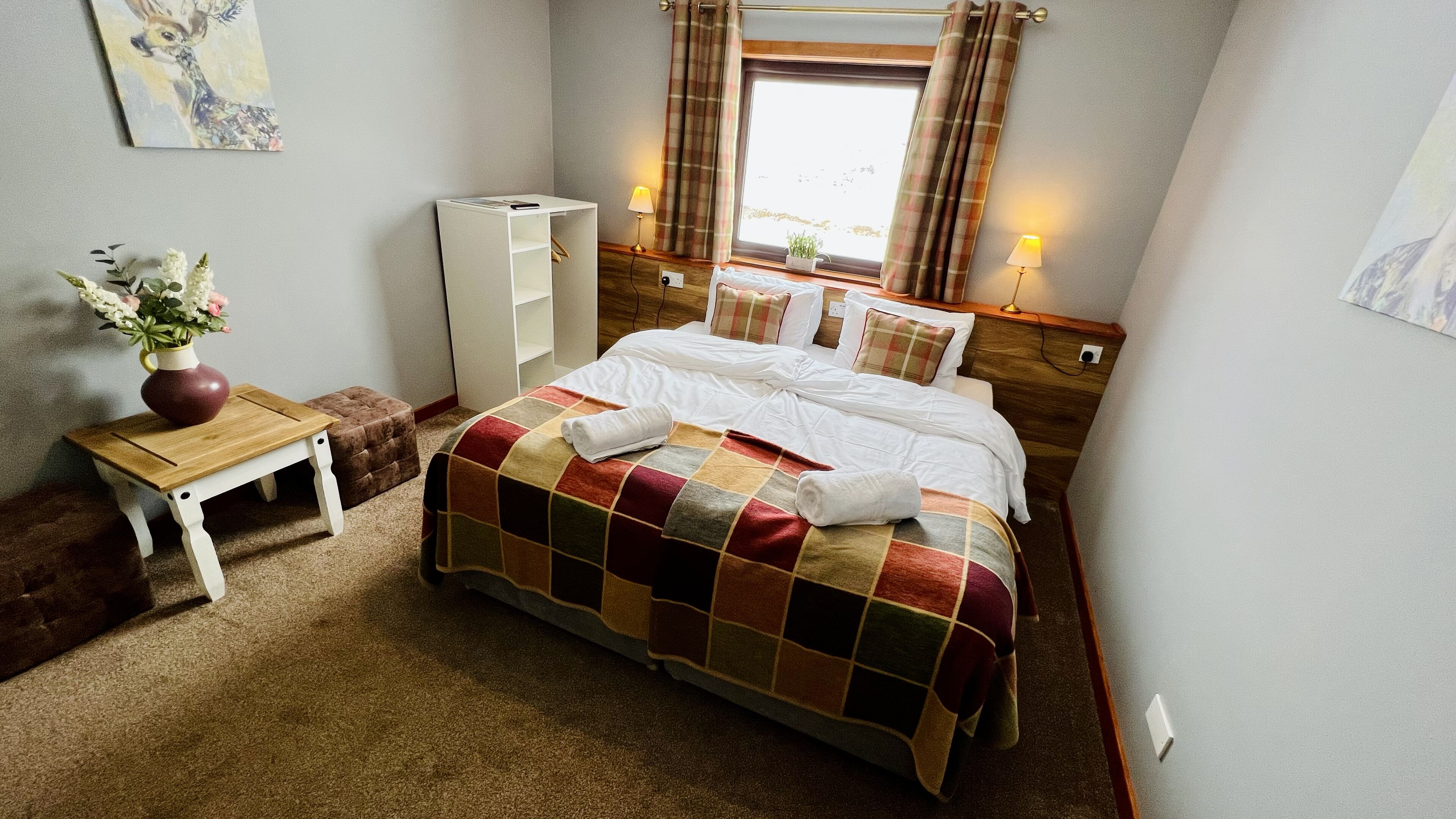 A neatly made bed with a checkered blanket, a bedside table with a vase of flowers, and a wardrobe.