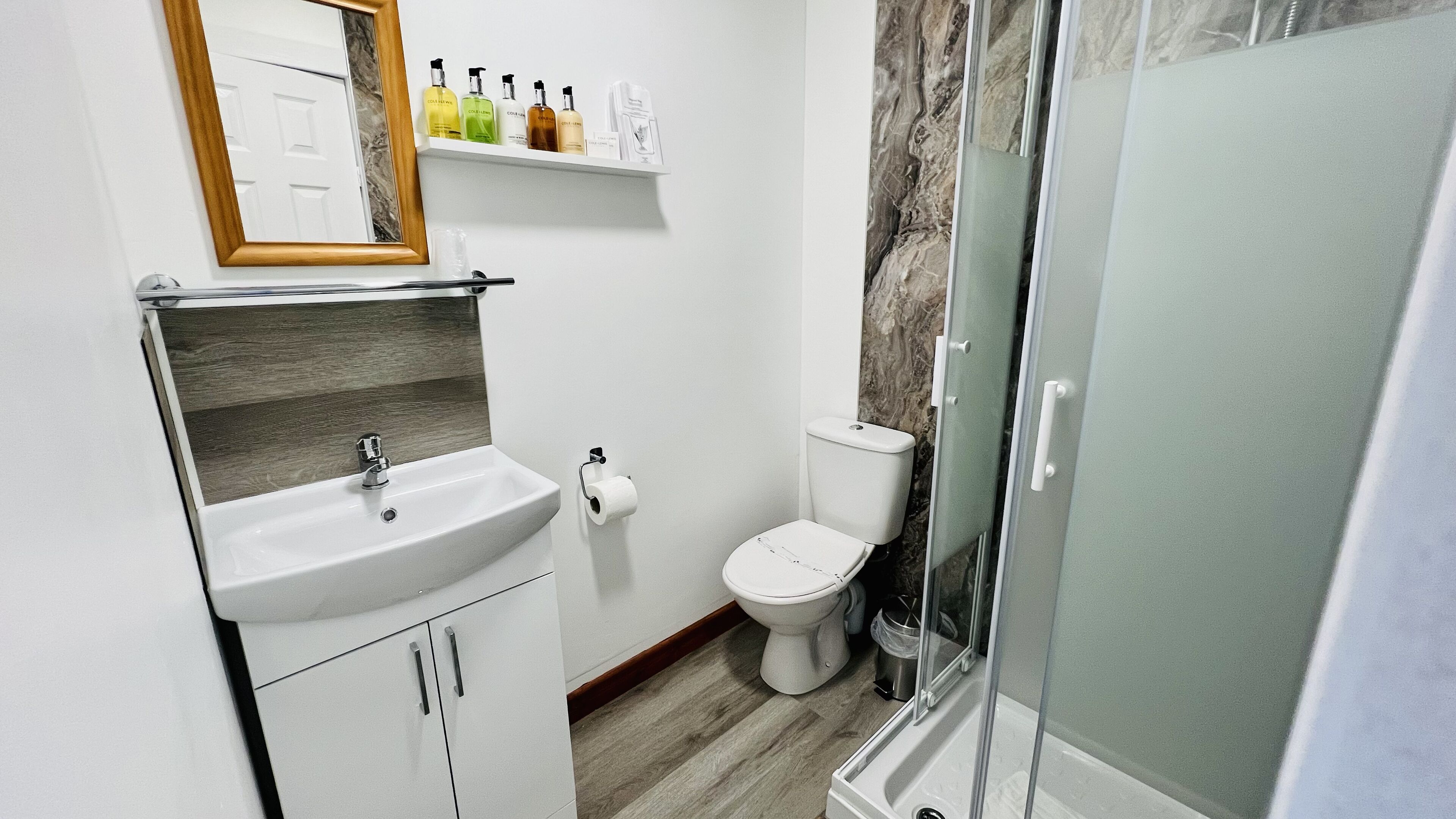 A bathroom with a sink, toilet, and shower. There are toiletries on a shelf above the sink.