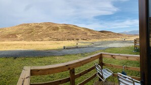 A wooden deck with a bench and a metal chair overlooking a river and a hilly landscape. - Aultguish Inn (Garve)