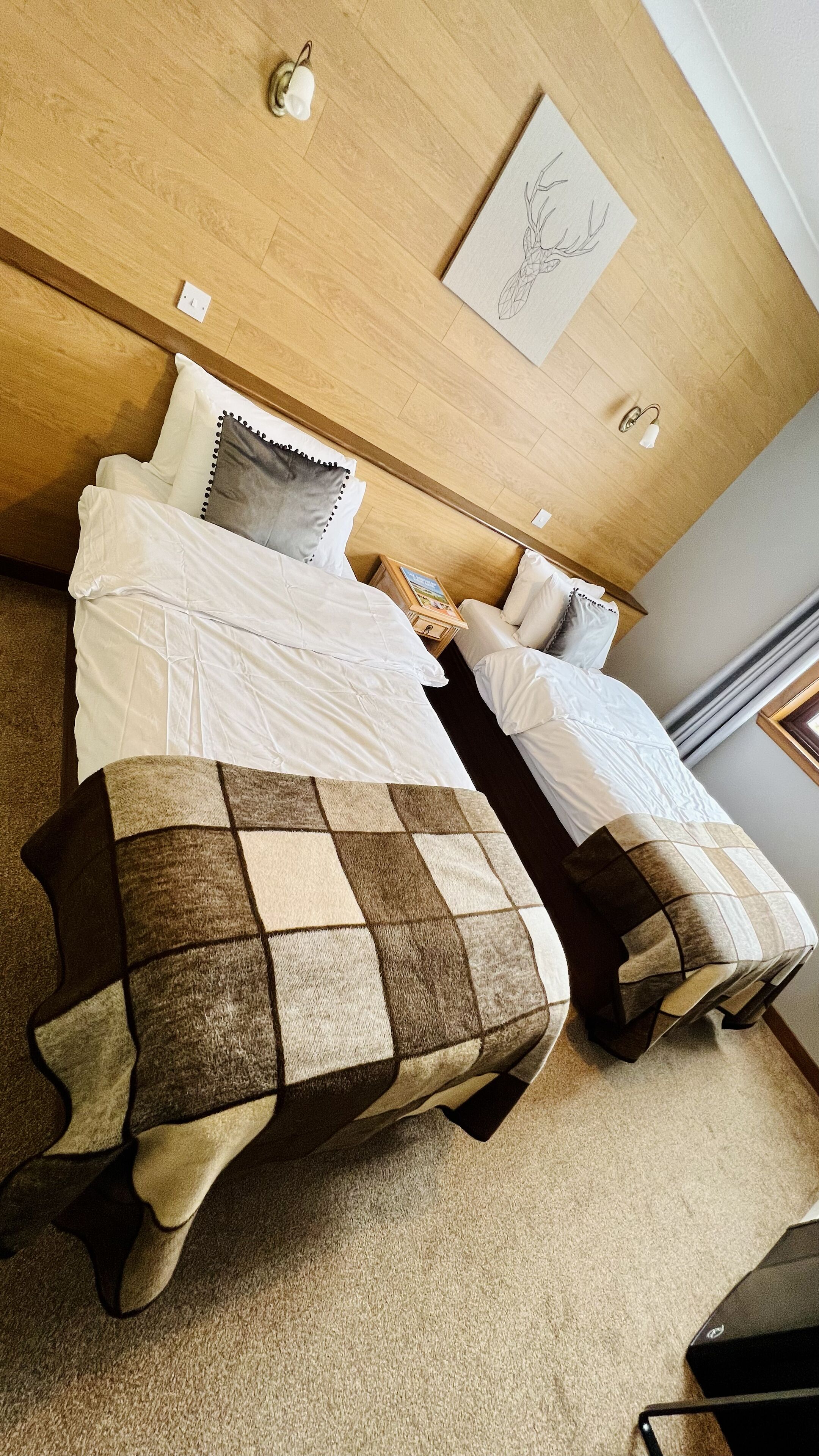 A hotel room with two beds, a wooden headboard, a small table with a picture frame, and a wall-mounted light fixture.