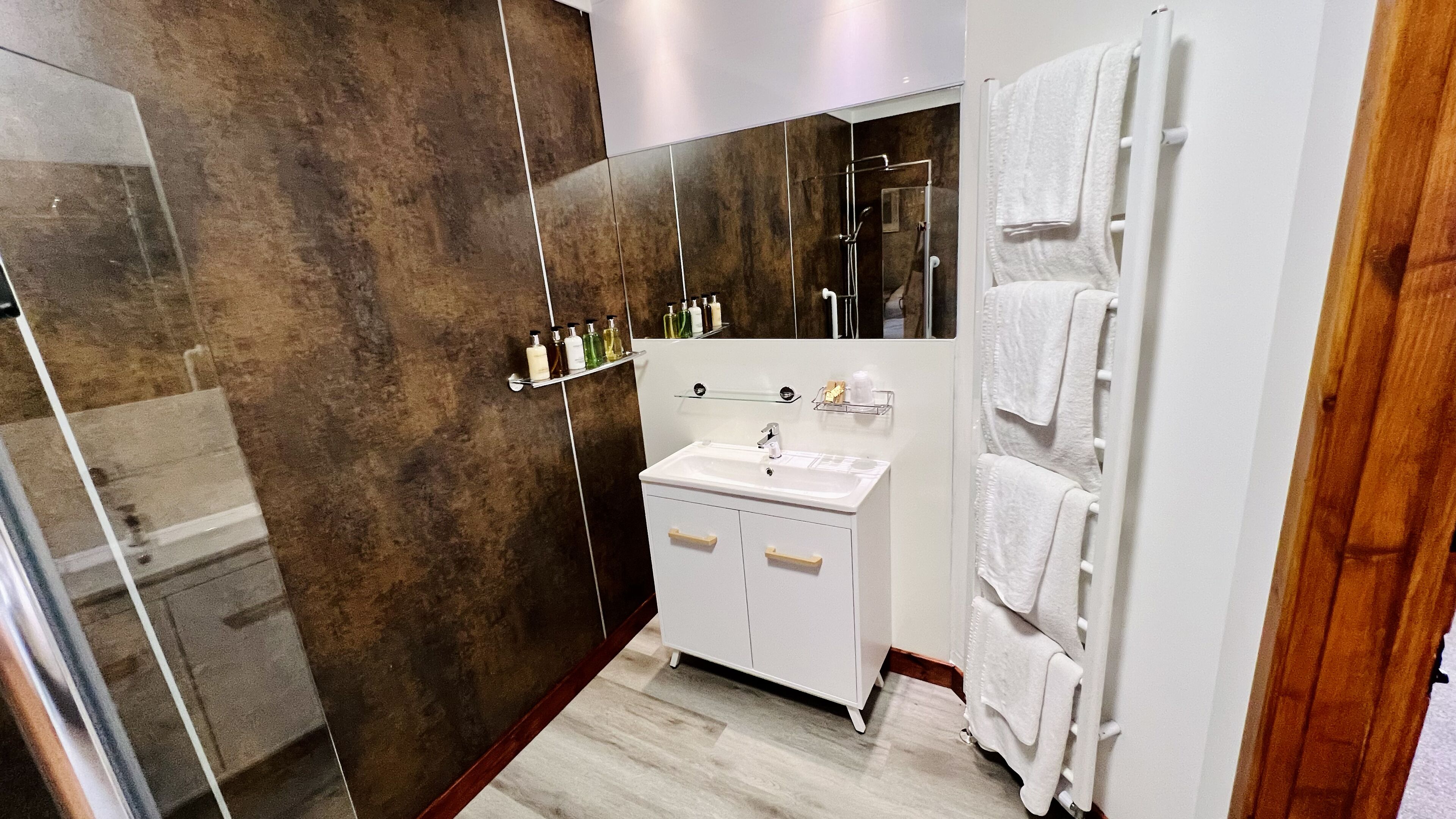 A modern bathroom with a walk-in shower, a white sink with a mirror above it, and a towel rack with multiple towels.