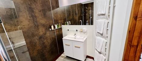 A modern bathroom with a walk-in shower, a white sink with a mirror above it, and a towel rack with multiple towels.
