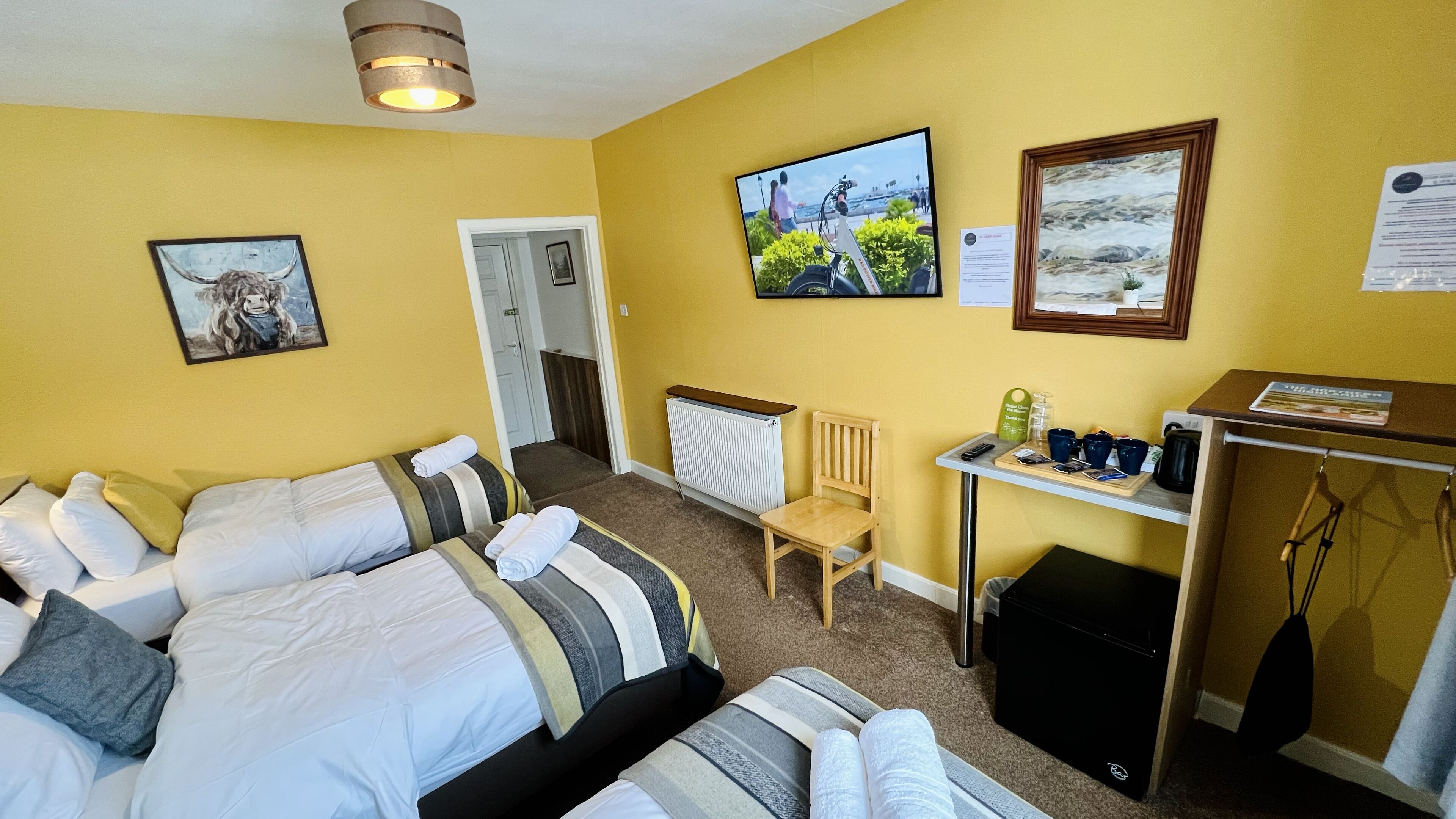 A hotel room with a bed, a chair, a small table with cups and a remote control, and a TV on the wall.