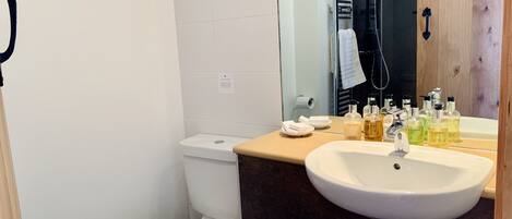 Ein Badezimmer mit einer weißen Toilette, einem Waschbecken mit Spiegel darüber und Toilettenartikeln auf dem Waschbecken.