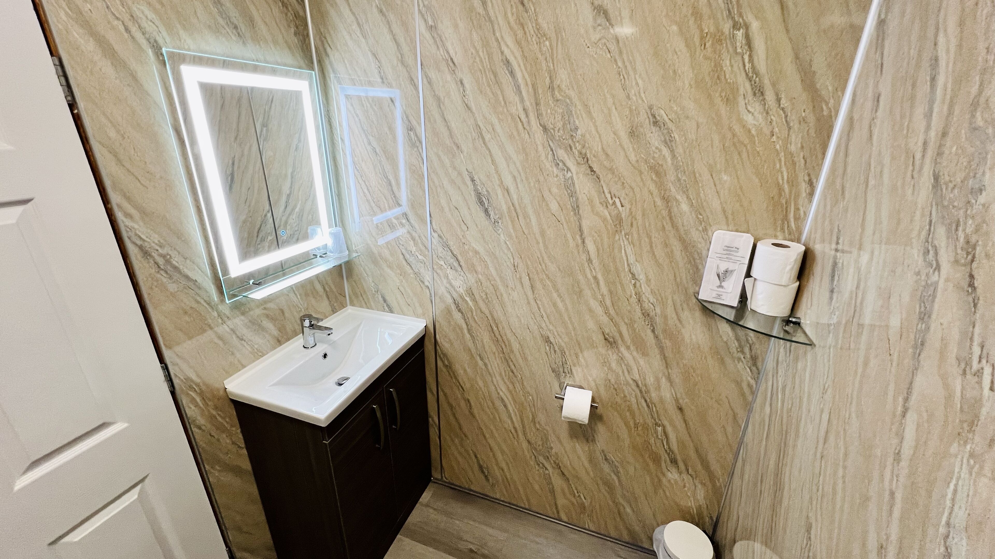Ein Badezimmer mit Marmorwand, Waschbecken, Spiegel und Toilette.
