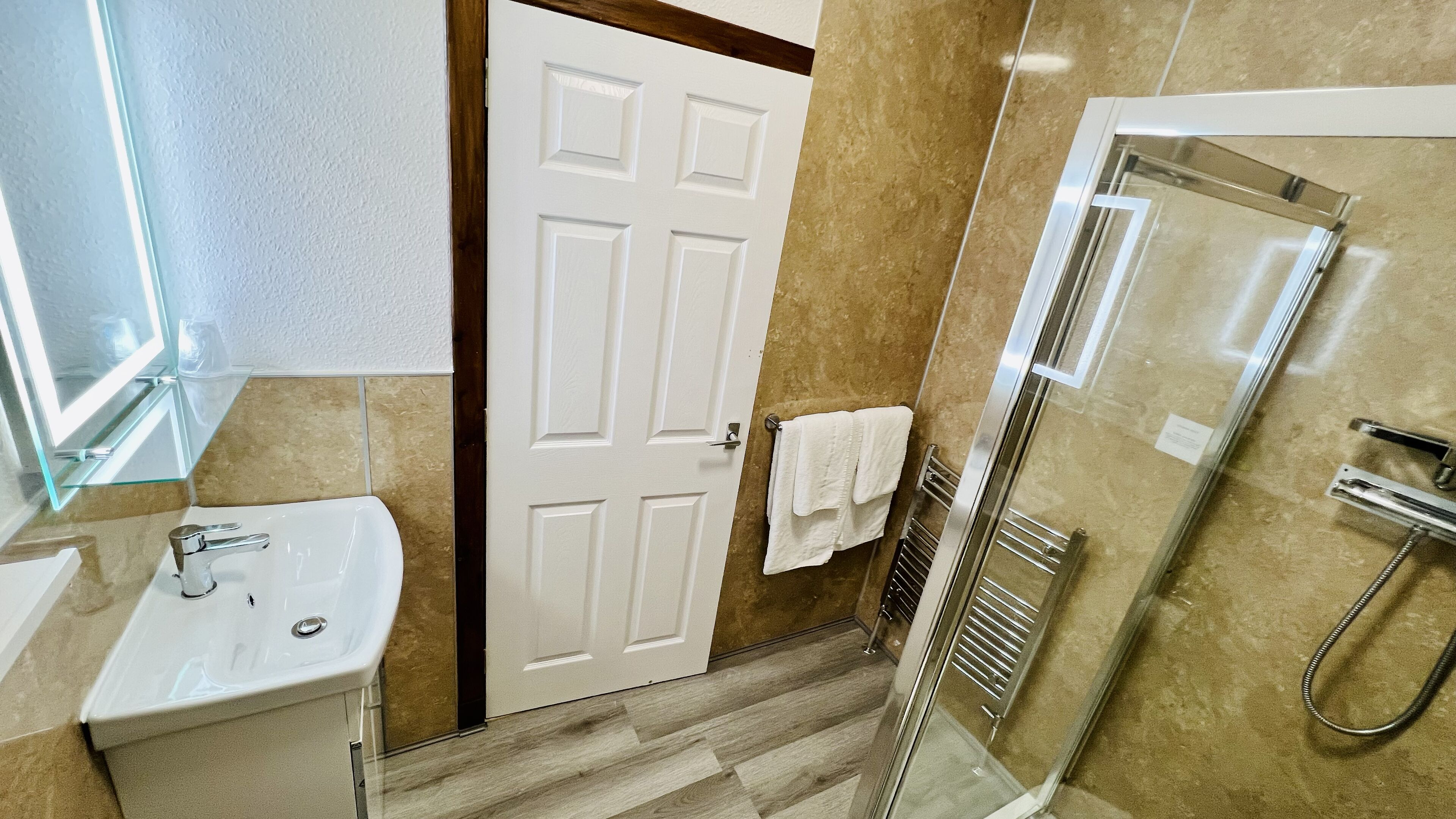 A bathroom with a white sink, a glass shower enclosure, and a door with a towel hanging on the handle.