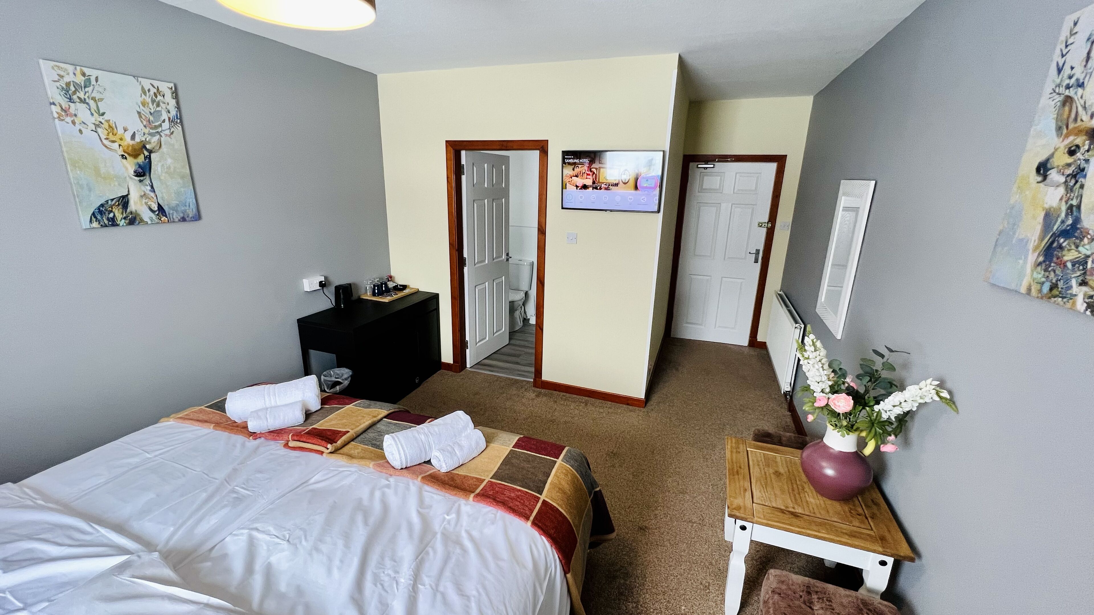 Une chambre d’hôtel avec un lit, un bureau, une télévision et une salle de bain, visibles à travers une porte ouverte.