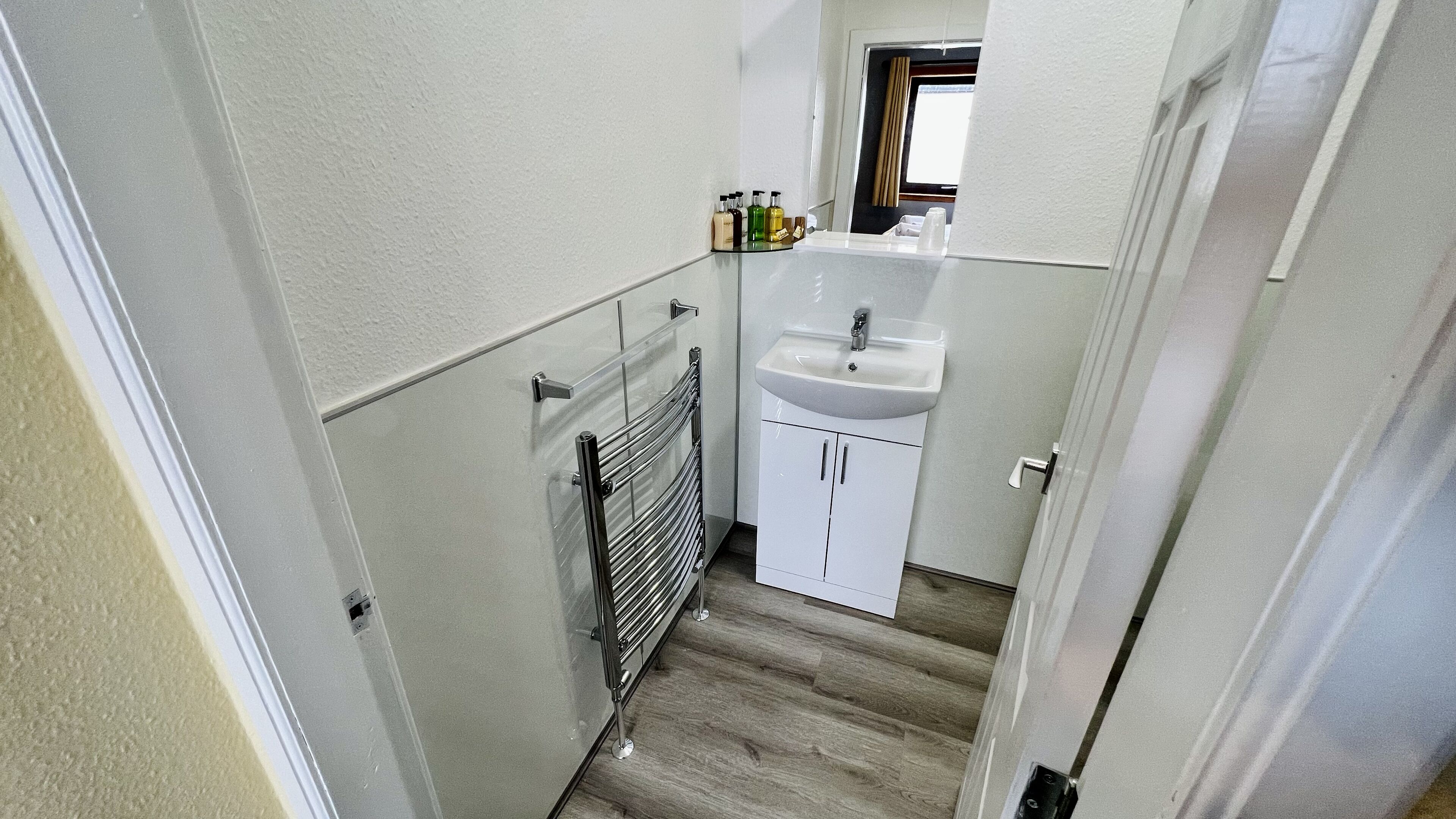 A compact bathroom with a white sink, a glass shower enclosure, and a small window.