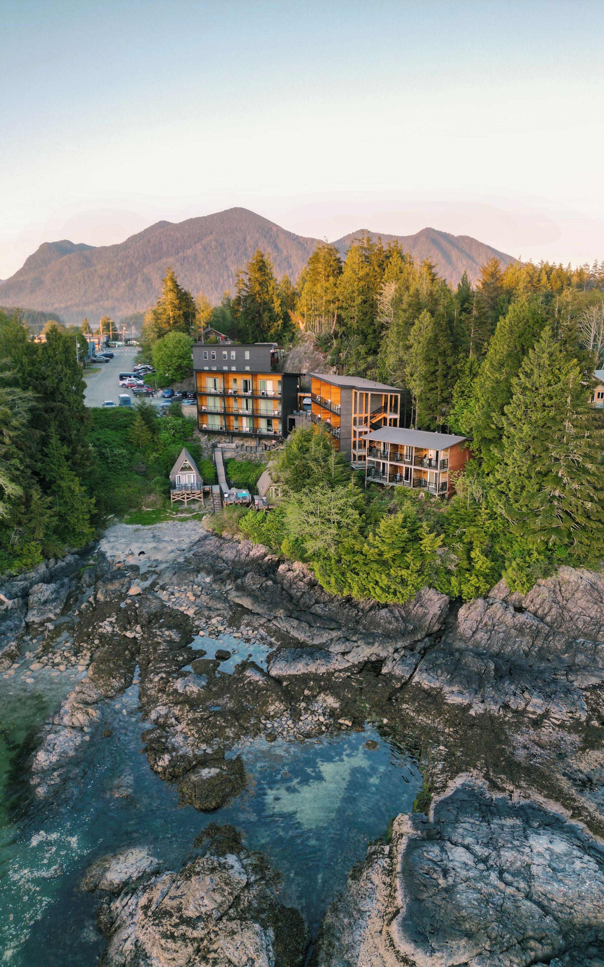 A multi-story building with balconies, surrounded by dense forest and mountains in the background.