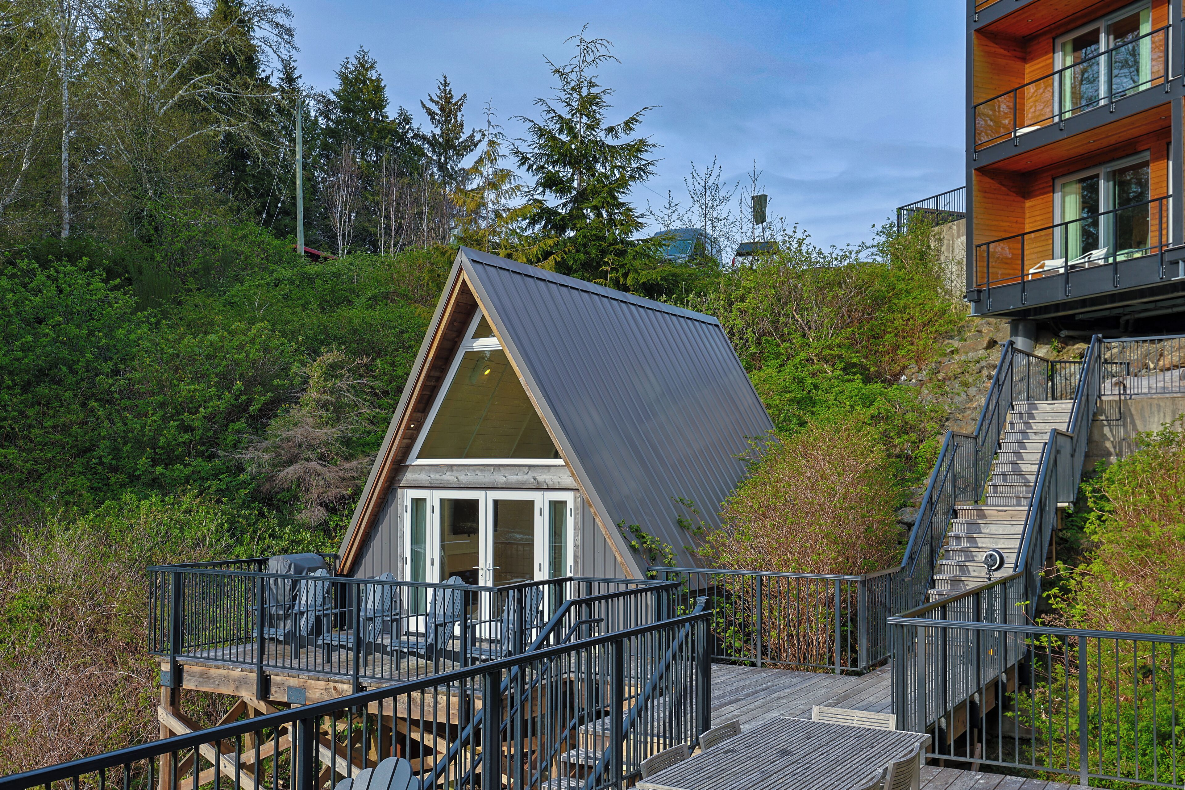 A modern house with a deck, a staircase, and a view of the surrounding forest.